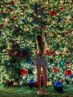 jong meisje Aan de achtergrond van de Kerstmis boom in miami. mooi Kerstmis boom Bij de populair Oppervlakte Bij Kerstmis vooravond en lichten foto