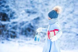 aanbiddelijk meisje met Kerstmis doos geschenk in winter buitenshuis Aan Kerstmis vooravond foto