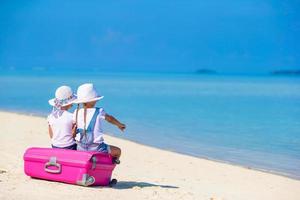 weinig toeristen meisjes met groot koffer Aan tropisch wit strand. reizen concept. foto