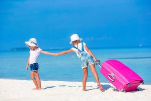 weinig toeristen meisjes met groot koffer Aan tropisch wit strand. reizen concept. foto