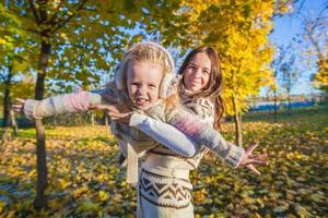 weinig aanbiddelijk meisje en jong moeder hebben pret in herfst park Aan zonnig dag foto