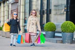 aanbiddelijk weinig meisjes met boodschappen doen Tassen wandelen in de stad buitenshuis foto