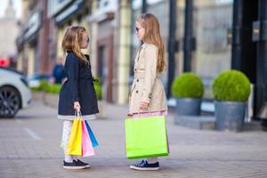 aanbiddelijk weinig meisjes met Tassen Aan boodschappen doen buitenshuis foto