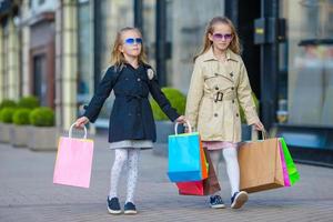 aanbiddelijk weinig meisjes Aan winkelen. portret van kinderen met boodschappen doen Tassen. foto