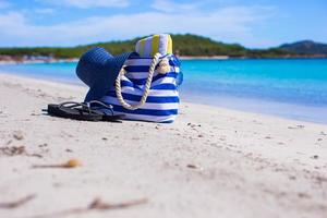 blauw tas, rietje hoed, omdraaien flops en handdoek Aan wit tropisch strand foto