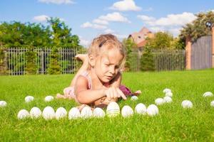 portret van weinig aanbiddelijk meisje spelen met wit Pasen eieren Aan groen gras foto