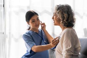 stethoscoop examen. aantrekkelijke vrolijke aziatische vrouwelijke arts die naar ouderen luistert tijdens het gebruik van een stethoscoop foto
