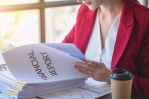 financieel, Aziatisch zakenvrouw in rood pak Holding kop van koffie zittend Aan bureau in kantoor, hebben computer voor aan het doen accounting werk Bij werkplaats naar berekenen jaar- winst door plicht, bedrijf idee foto