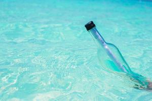 fles met een bericht in de hand- achtergrond blauw lucht foto