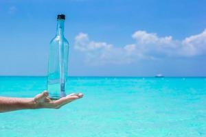 fles met een bericht in de hand- achtergrond blauw lucht foto