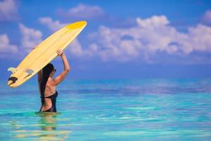 gelukkig welgevormd surfen vrouw Bij wit strand met geel surfboard foto