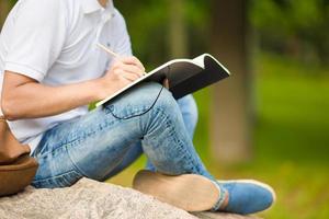 dichtbij omhoog van handen van jongen aan het studeren voor college tentamen in park buiten foto