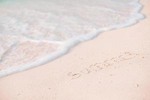 woord zomer handgeschreven Aan zanderig strand met zacht oceaan Golf Aan achtergrond foto