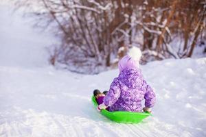 weinig schattig meisje trekt een slee in warm winter dag foto