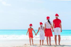 gelukkig familie in rood de kerstman hoeden Aan een tropisch strand vieren Kerstmis vakantie foto
