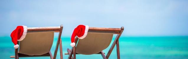 zon ligstoelen met de kerstman hoed Bij tropisch strand met wit zand en turkoois water foto
