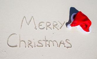 vrolijk Kerstmis geschreven Aan tropisch strand wit zand met Kerstmis hoed foto