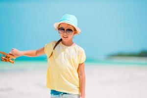 gelukkig weinig meisje met speelgoed- vliegtuig in handen Aan wit zanderig strand. foto