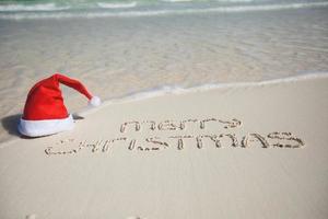 vrolijk Kerstmis geschreven Aan tropisch strand wit zand met Kerstmis hoed foto