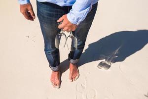 detailopname van twee bril in hand- Bij Mens wandelen blootsvoets Aan wit strand foto