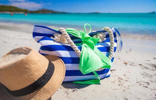 streep tas, rietje hoed, sunblock en handdoek Aan wit tropisch strand foto