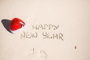 gelukkig nieuw jaar geschreven in de zand en de kerstman hoed Aan wit zanderig strand foto