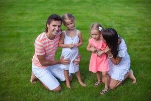 portret jong familie van vier zitten Aan de gras en hebben pret foto