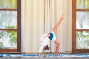 weinig meisje aan het doen yoga oefening Aan terras buitenshuis foto