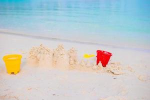 Zandkasteel Aan wit strand met plastic kinderen speelgoed foto