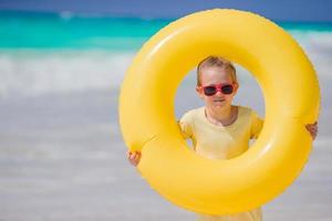 portret van weinig meisje met opblaasbaar rubber cirkel Aan strand vakantie foto