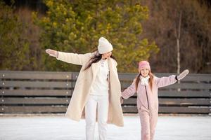 weinig aanbiddelijk meisje met haar moeder het schaatsen Aan ijsbaan foto