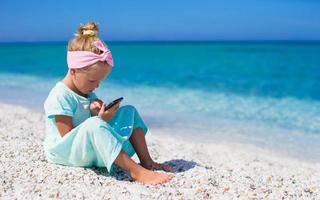 weinig schattig meisje nemen afbeeldingen Aan telefoon Bij tropisch strand foto