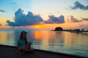 silhouet van schattig klein meisje op houten steiger bij zonsondergang foto