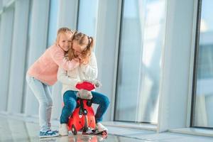 schattige kleine meisjes plezier op de luchthaven zittend op koffer te wachten op instappen foto