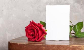 rood roos met wit papier vel voor tekst Aan oud rustiek houten tafel Aan licht beton muur backdrop foto