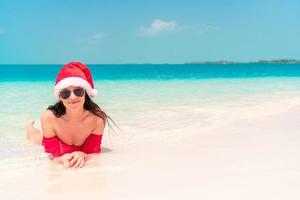 jong gelukkig vrouw in de kerstman hoed in zwempak Aan wit strand Aan Kerstmis vakantie foto