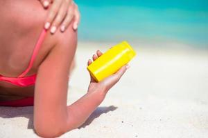 mooi jong vrouw Holding een zonnecreme aan het liegen Aan tropisch strand foto