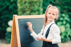 gelukkig weinig schoolmeisje met een schoolbord buitenshuis foto