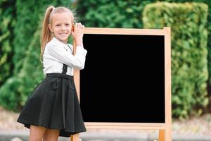 gelukkig weinig schoolmeisje met een schoolbord buitenshuis foto