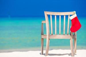 rood de kerstman hoed Aan stoel Bij tropisch wit strand foto