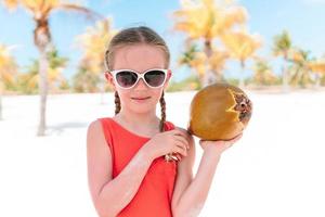 weinig aanbiddelijk meisje met groot kokosnoot Aan zanderig strand foto