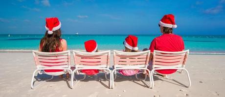 gelukkig familie van vier in Kerstmis hoeden Aan wit strand foto