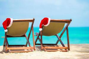 zon ligstoelen met de kerstman hoed Bij mooi tropisch strand met wit zand en turkoois water. perfect Kerstmis vakantie foto