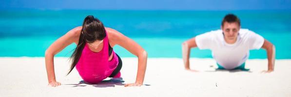 jong geschiktheid paar aan het doen Opdrukken gedurende buitenshuis kruis opleiding training Aan tropisch strand foto