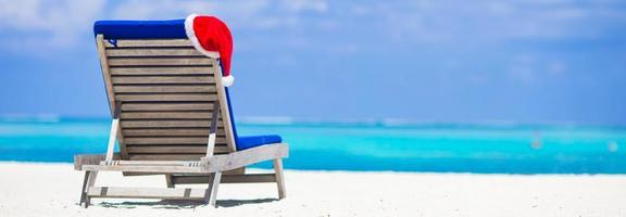 zon stoel ligstoel met rood de kerstman hoed Aan tropisch wit strand en turkoois water foto