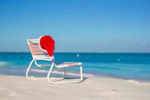 rood de kerstman hoed Aan stoel longue Bij tropisch strand foto