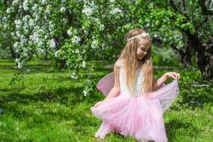 weinig schattig meisje met vlinder Vleugels in bloeiende appel boomgaard foto