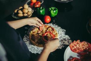 close-up van een vrouw toppings op zelfgemaakte pizza te zetten foto