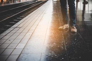 voeten van een jonge man met spijkerbroek te wachten op de trein foto