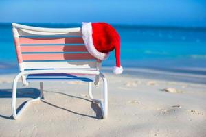 dichtbij omhoog de kerstman hoed Aan stoel longue Bij tropisch strand foto